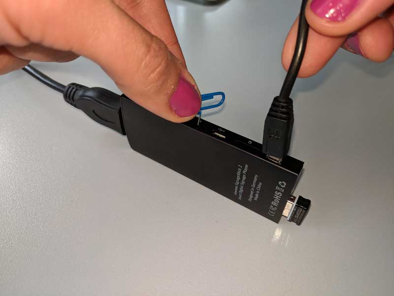 Clip presionando el botón de reinicio en el orificio del SignageStick